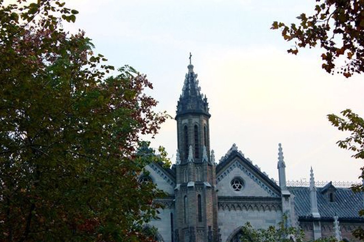 A historic brick church partly framed by leafy trees.